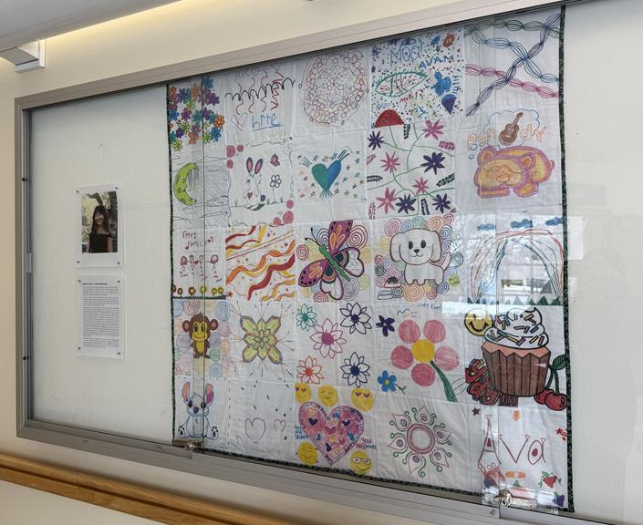 Glass display box featuring photo of Sydney Chon and her artist's statement (on the left) and the quilt itself on the right