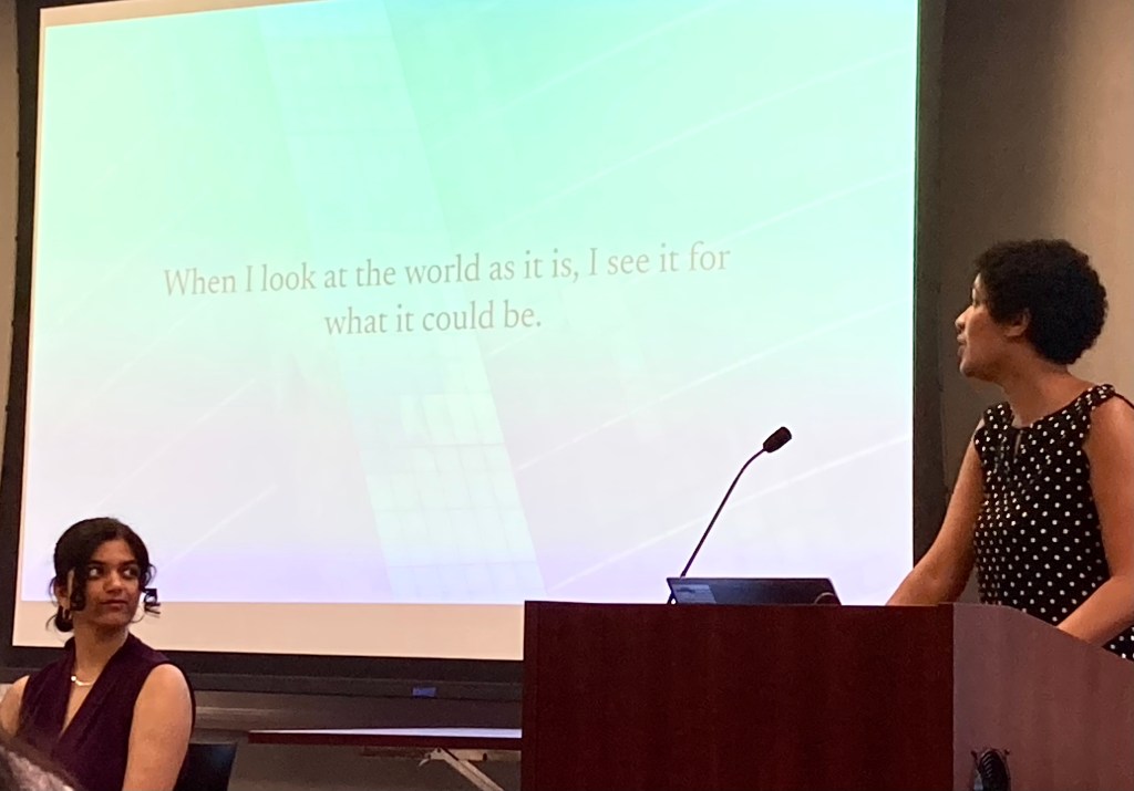 Avani Ghosh '26 (seated) and Sonam Sulman '26 (standing at podium) in front of a projected slide: When I look at the world as it is, I see it for what it could be."